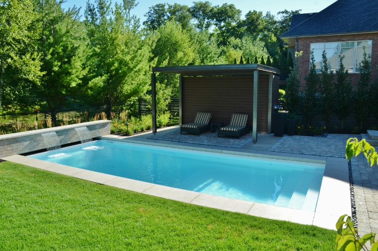 This is an example of a large modern back rectangular natural swimming pool in Toronto with a water feature and brick paving.