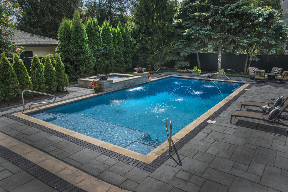 Ejemplo de piscina con fuente clásica de tamaño medio rectangular en patio trasero con adoquines de piedra natural