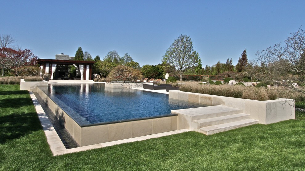 Réalisation d'une piscine à débordement et arrière minimaliste de taille moyenne et rectangle avec un bain bouillonnant et des pavés en pierre naturelle.