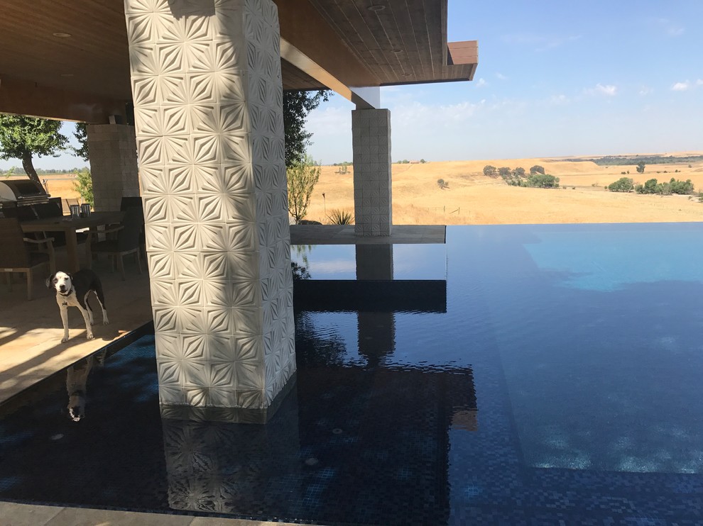 Photo of a large retro back rectangular infinity swimming pool in Other with a water feature and concrete paving.