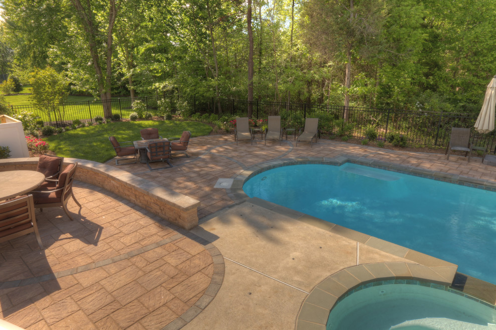 Diseño de piscina natural tradicional grande redondeada en patio trasero con adoquines de hormigón