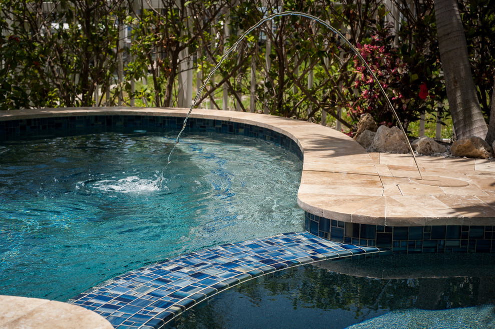 Ejemplo de piscinas y jacuzzis tropicales de tamaño medio a medida en patio trasero con adoquines de piedra natural