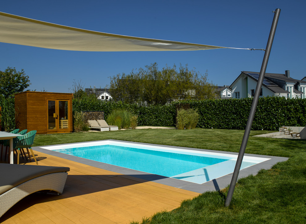 Modelo de piscina moderna de tamaño medio rectangular en patio lateral con losas de hormigón