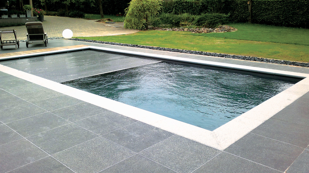 Foto de piscina alargada actual grande rectangular en patio trasero con suelo de baldosas