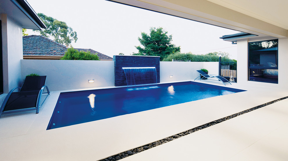 Ejemplo de piscina alargada contemporánea grande rectangular en patio trasero con suelo de baldosas