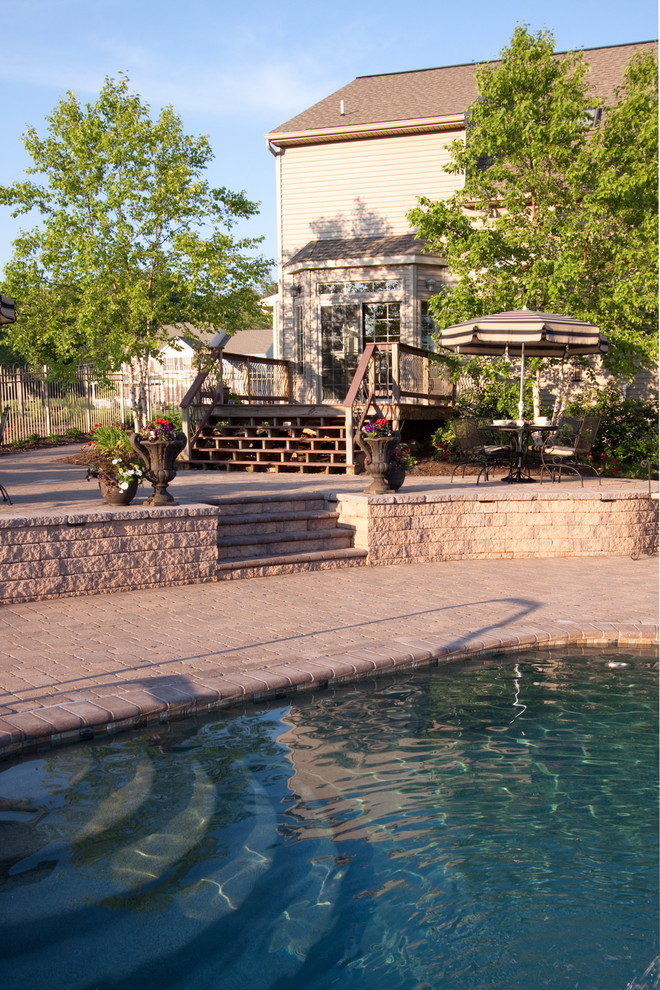 Idée de décoration pour une grande piscine arrière tradition sur mesure avec un bain bouillonnant et des pavés en pierre naturelle.