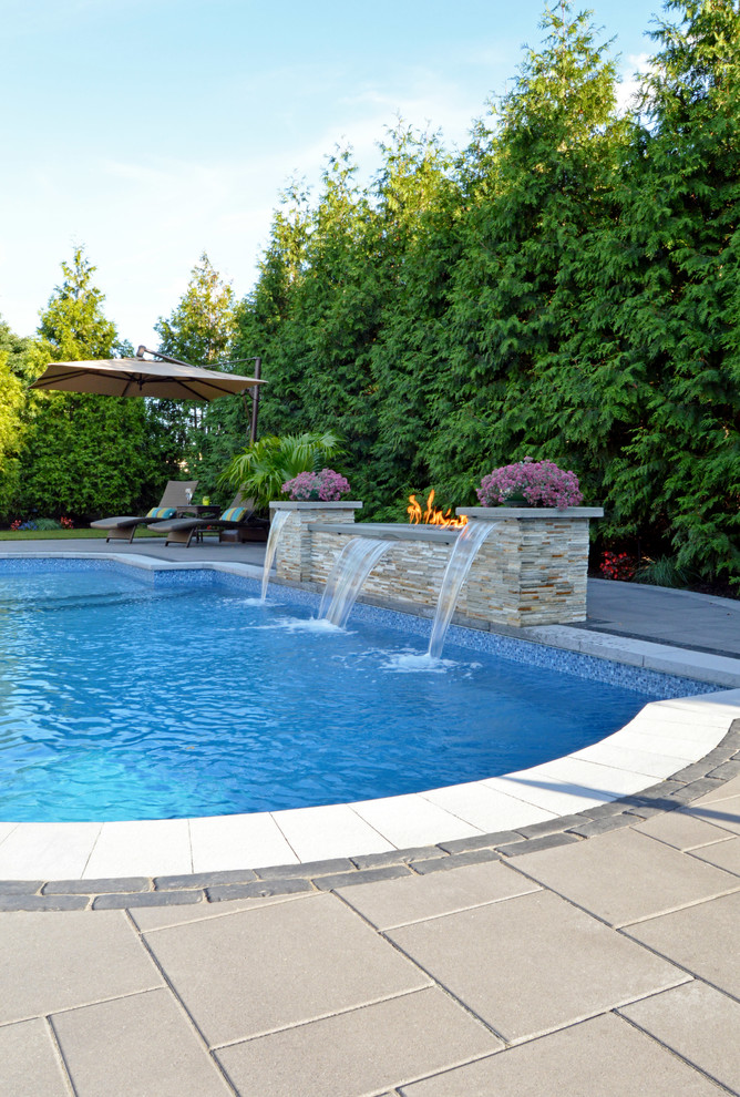 Modelo de piscina actual rectangular en patio trasero con adoquines de hormigón