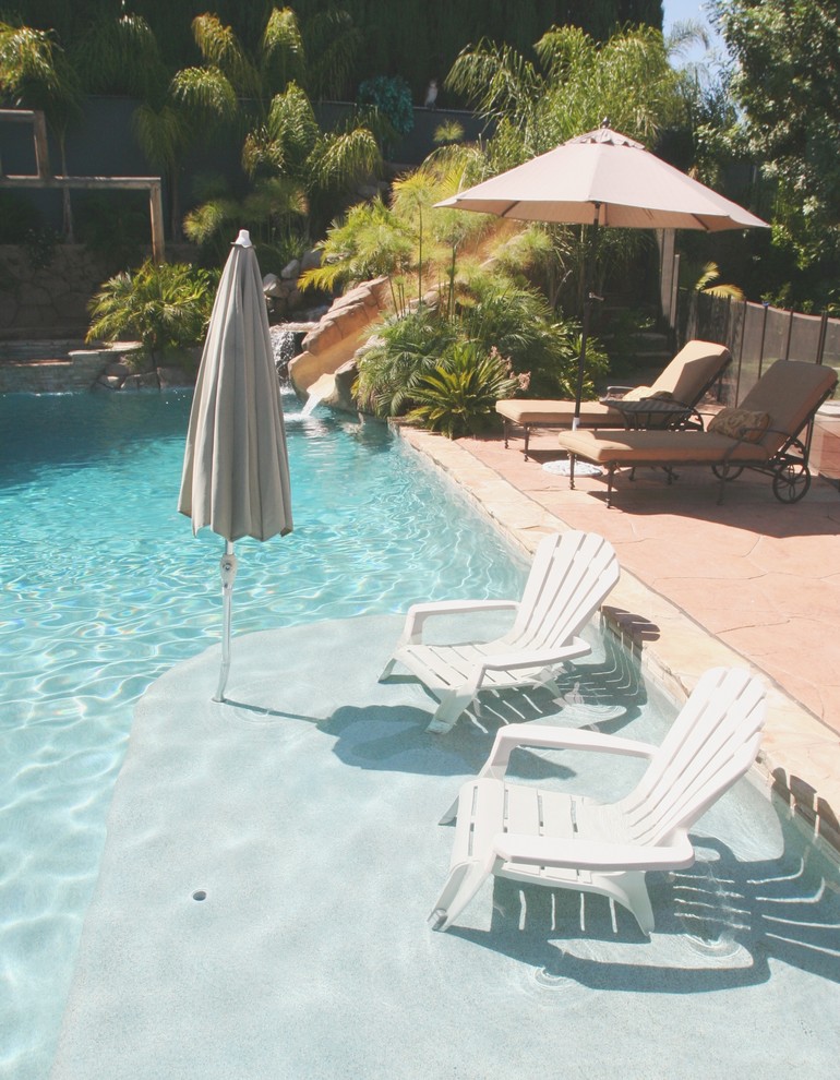 Immagine di una piscina monocorsia tropicale personalizzata di medie dimensioni e dietro casa con un acquascivolo e pavimentazioni in pietra naturale