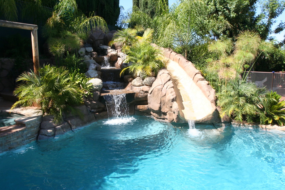Medium sized world-inspired back custom shaped lengths swimming pool in Los Angeles with a water slide and natural stone paving.