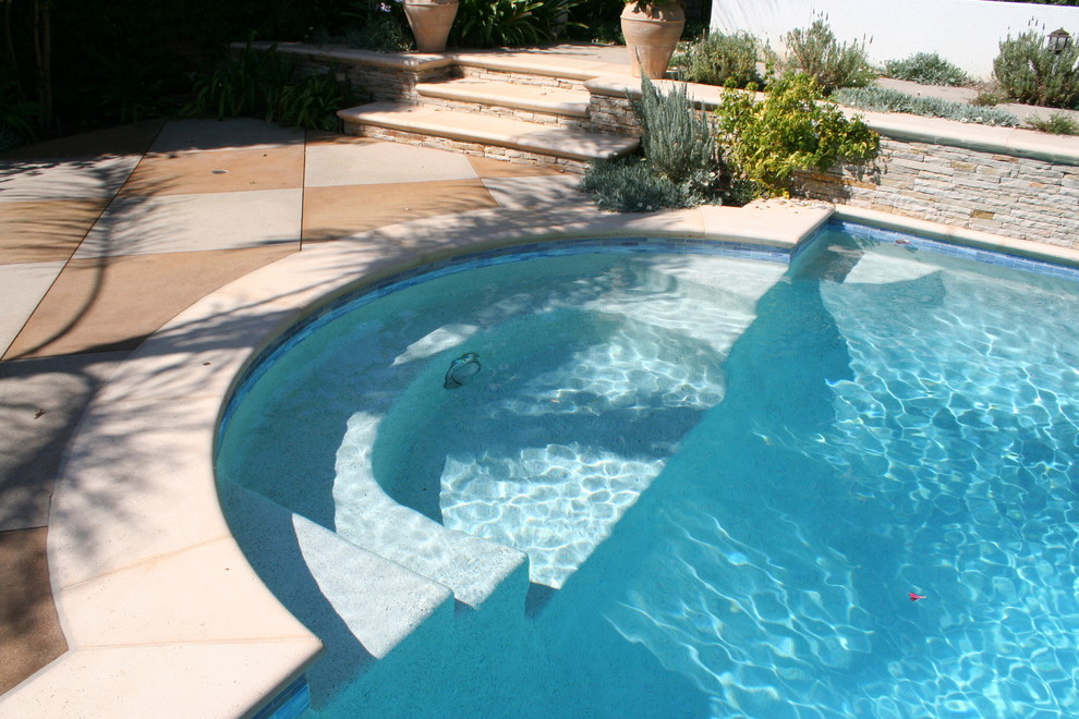 На фото: спортивный бассейн среднего размера, произвольной формы на заднем дворе в средиземноморском стиле с джакузи и покрытием из бетонных плит с