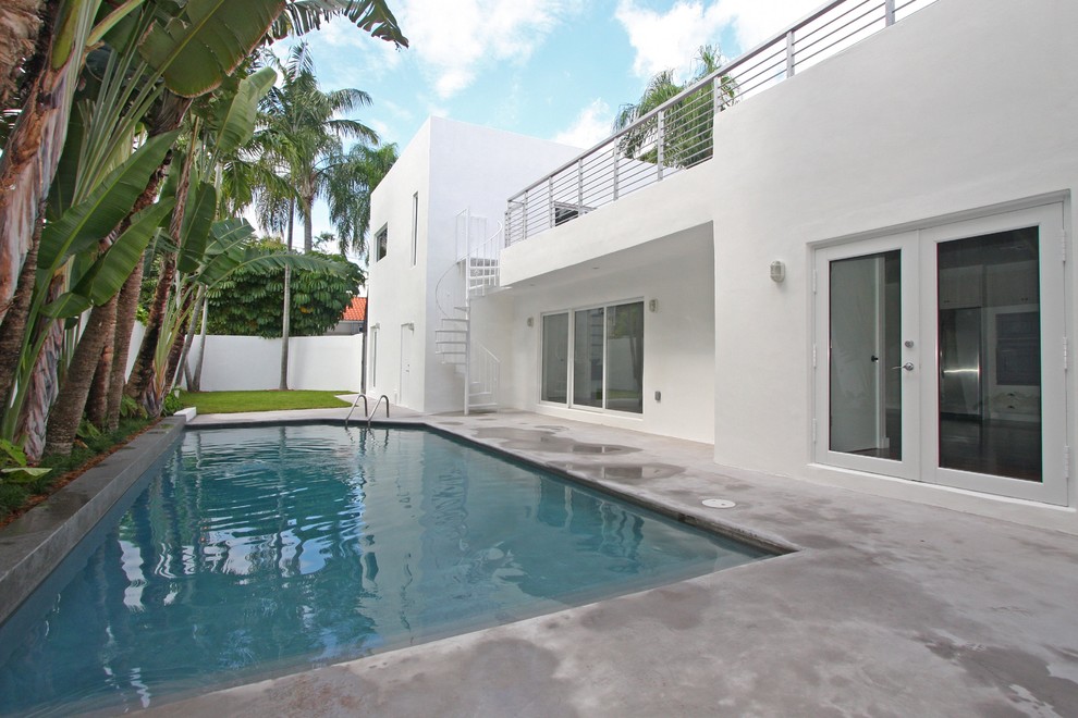 Modern back rectangular swimming pool in Miami with concrete slabs.