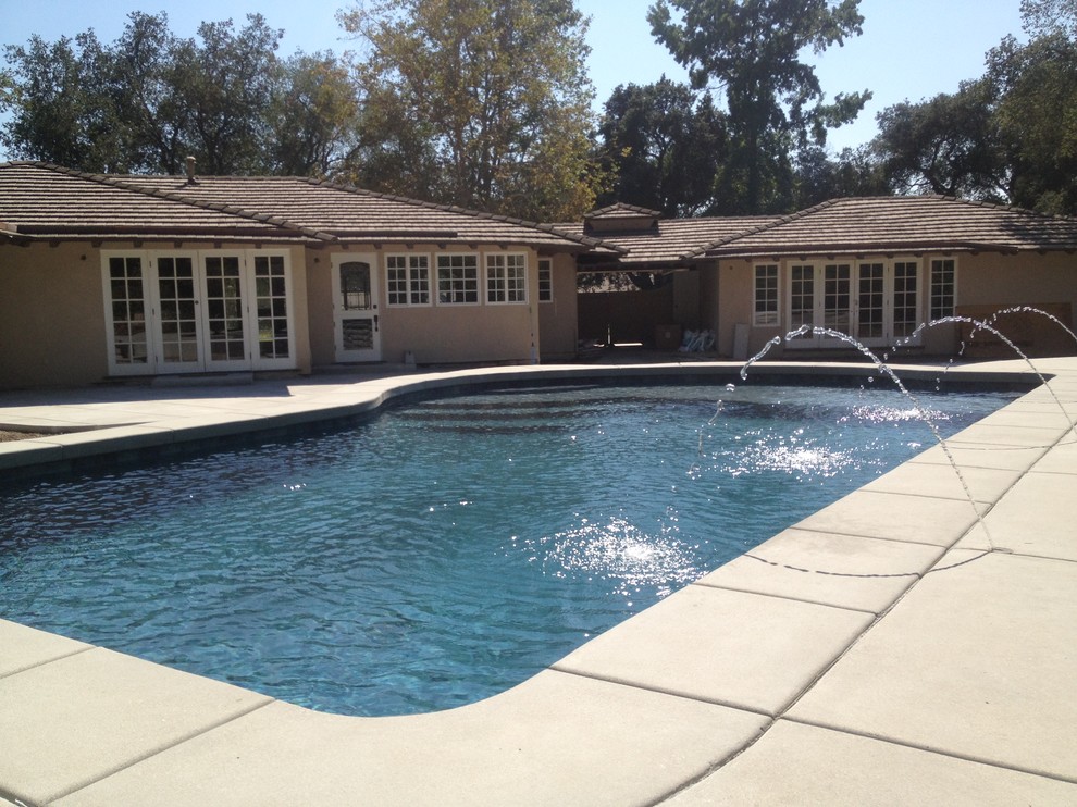 Großer Moderner Schwimmteich hinter dem Haus in rechteckiger Form mit Wasserspiel und Betonboden in Los Angeles