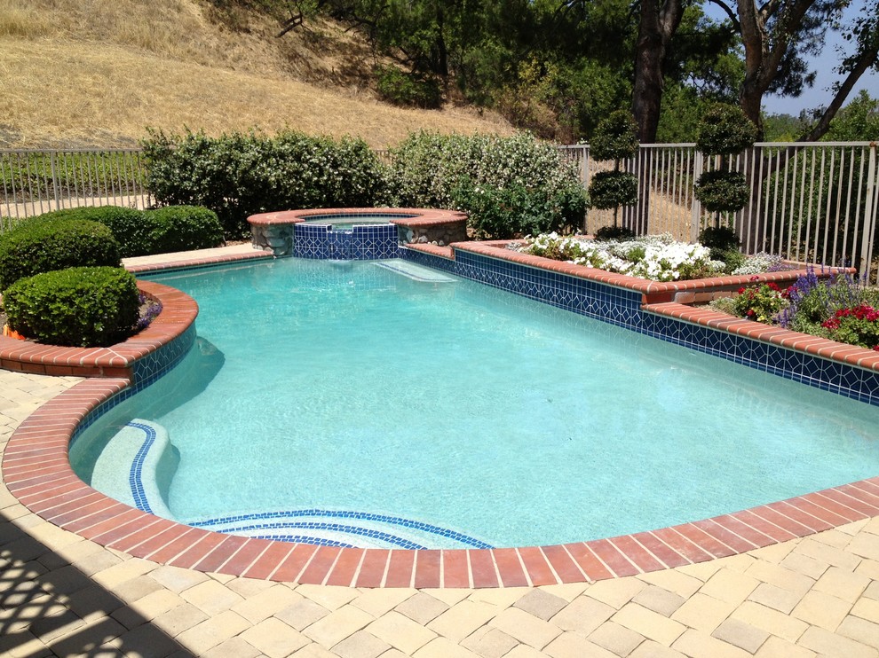 На фото: естественный бассейн среднего размера, произвольной формы на заднем дворе в средиземноморском стиле с джакузи и мощением клинкерной брусчаткой
