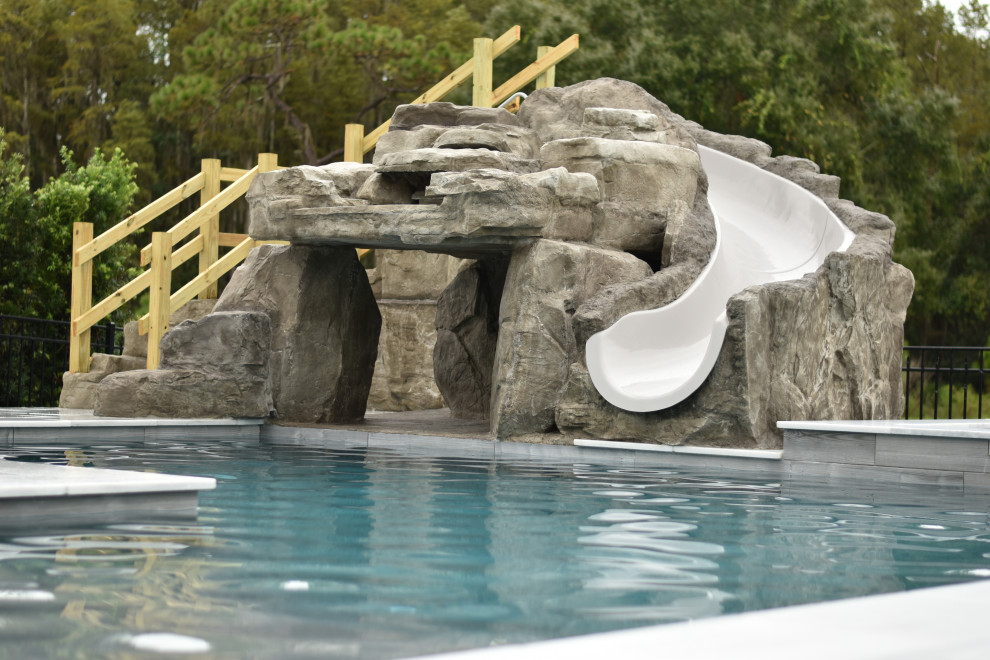 Ejemplo de piscina con tobogán contemporánea grande a medida en patio trasero con adoquines de piedra natural