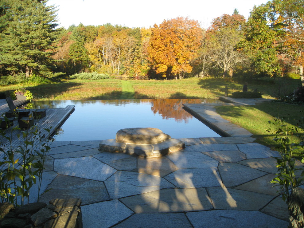 Ejemplo de piscina infinita tradicional de tamaño medio a medida en patio trasero con adoquines de piedra natural