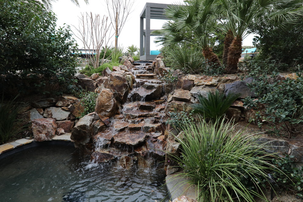 Ejemplo de piscina con fuente natural exótica extra grande a medida en patio trasero con adoquines de piedra natural
