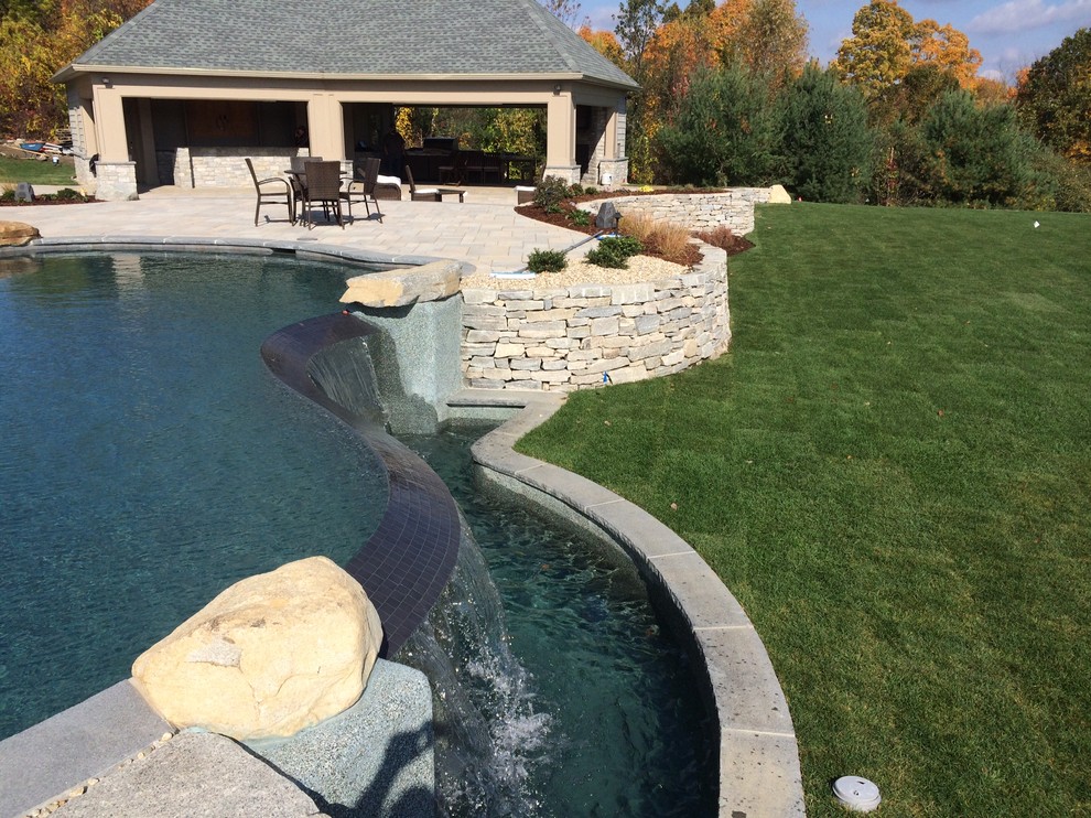 Ispirazione per un'ampia piscina a sfioro infinito classica personalizzata dietro casa con una dépendance a bordo piscina e pavimentazioni in cemento