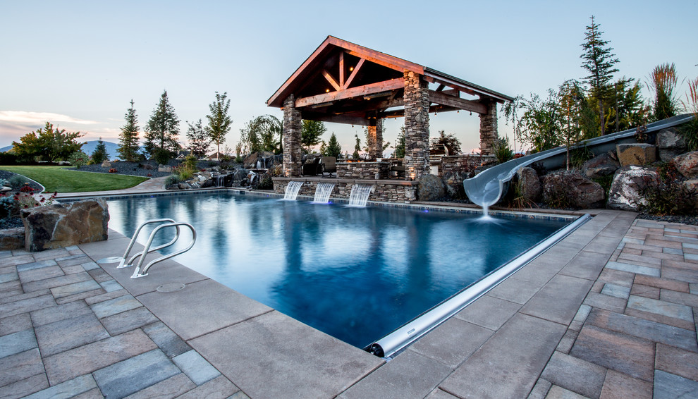 Ejemplo de piscina con tobogán rústica de tamaño medio rectangular en patio trasero con adoquines de hormigón