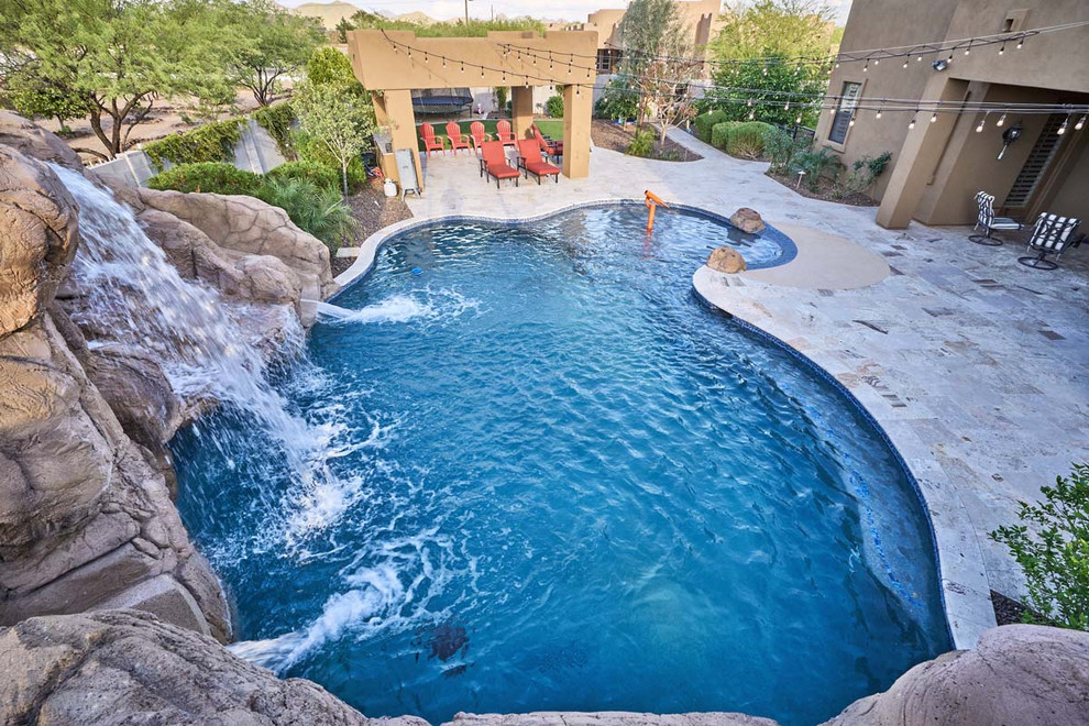 Foto di una grande piscina naturale tropicale personalizzata dietro casa con un acquascivolo e pavimentazioni in pietra naturale