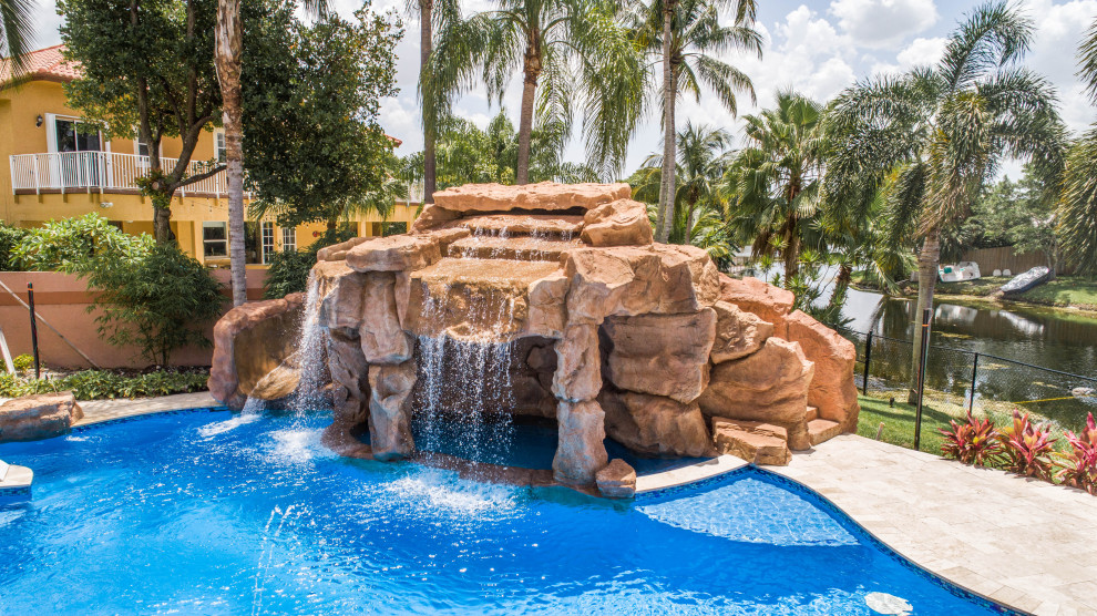 Idée de décoration pour une très grande piscine naturelle et arrière ethnique sur mesure avec un toboggan et des pavés en pierre naturelle.