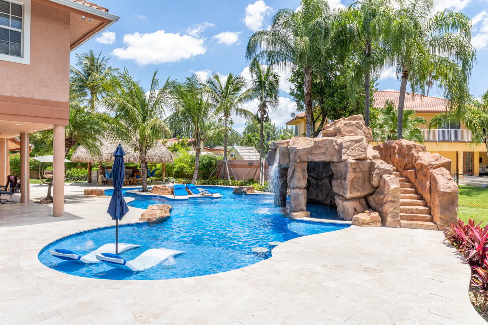 Immagine di un'ampia piscina naturale tropicale personalizzata dietro casa con un acquascivolo e pavimentazioni in pietra naturale