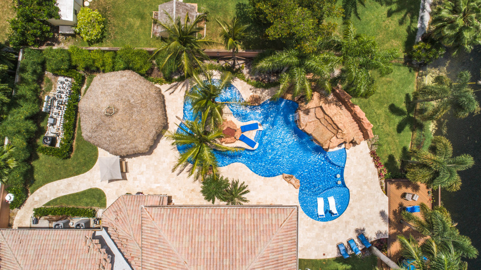 This is an example of an expansive world-inspired back custom shaped natural swimming pool in Miami with a water slide and natural stone paving.