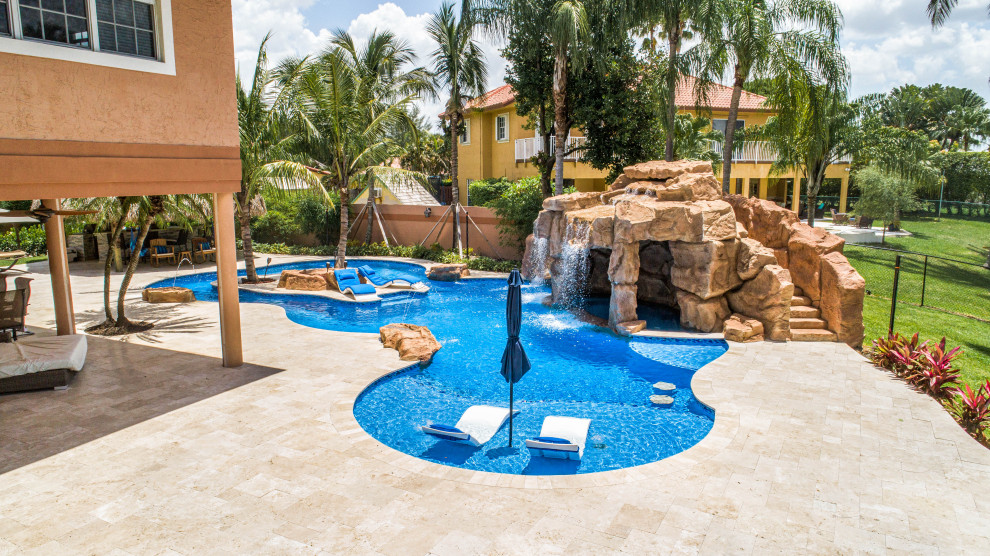 Ispirazione per un'ampia piscina naturale tropicale personalizzata dietro casa con un acquascivolo e pavimentazioni in pietra naturale