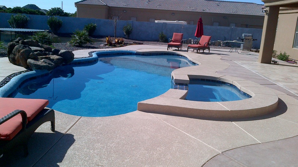 Esempio di una piscina stile americano personalizzata di medie dimensioni e dietro casa con una vasca idromassaggio e lastre di cemento