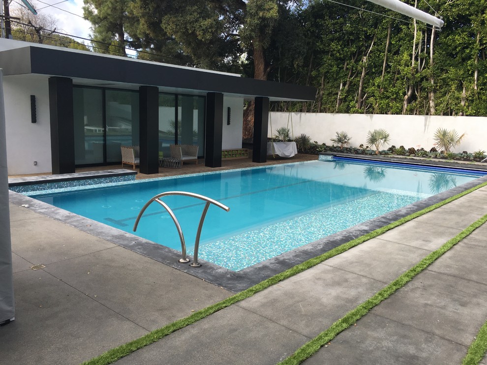 Diseño de piscina infinita moderna grande rectangular en patio trasero con suelo de baldosas