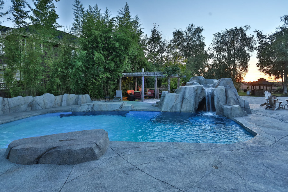 Design ideas for an expansive beach style back custom shaped natural swimming pool in Vancouver with a water feature and concrete slabs.