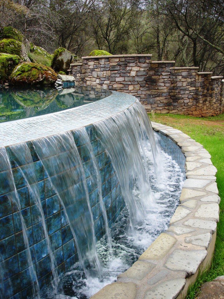Cette image montre une grande piscine à débordement et arrière chalet sur mesure avec un point d'eau et des pavés en pierre naturelle.