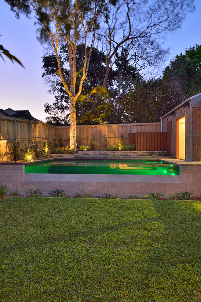 This is an example of a large contemporary back custom shaped above ground swimming pool in Sydney with a pool house and natural stone paving.