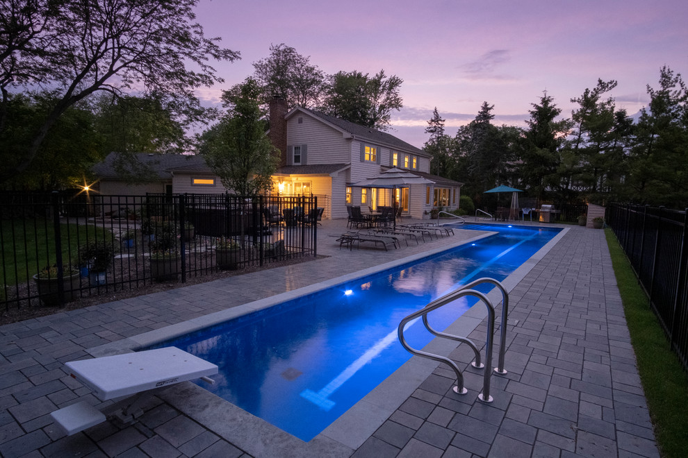 Modelo de piscina alargada clásica grande en forma de L en patio trasero con adoquines de hormigón