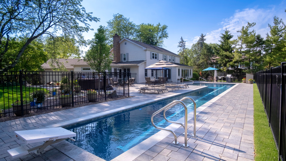 Diseño de piscina alargada clásica grande en forma de L en patio trasero con adoquines de hormigón