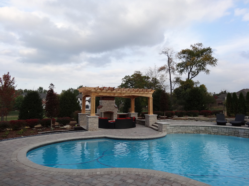 На фото: большой естественный бассейн произвольной формы на заднем дворе в классическом стиле с джакузи и мощением тротуарной плиткой с