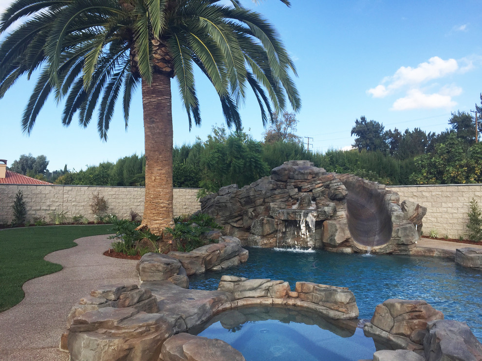 Ejemplo de piscina con tobogán natural exótica grande a medida en patio trasero