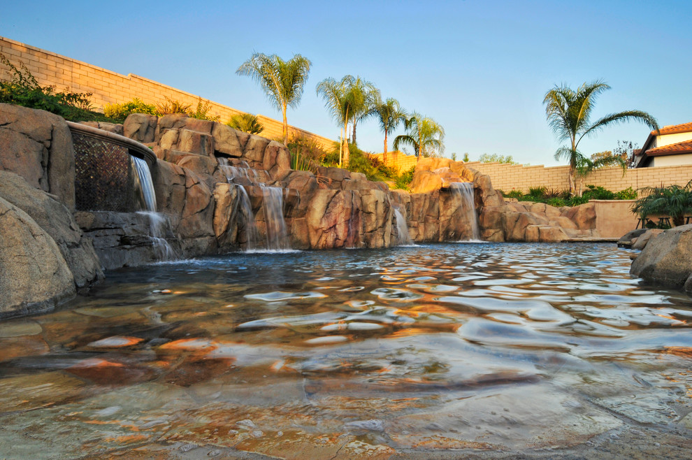 Immagine di una grande piscina naturale tropicale personalizzata dietro casa con una vasca idromassaggio e lastre di cemento