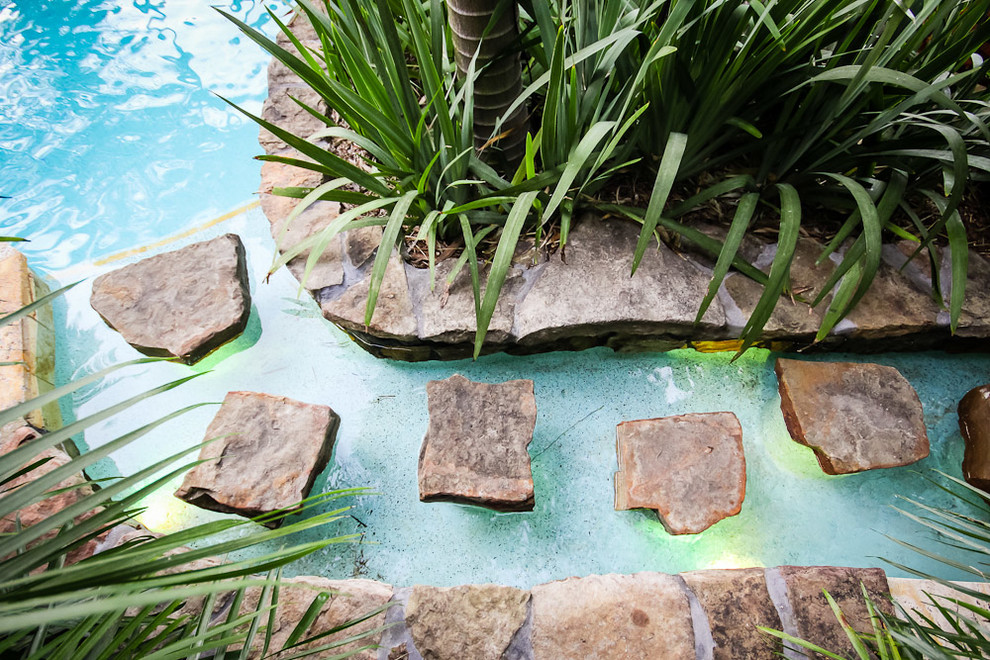 Ispirazione per un'ampia piscina monocorsia tropicale personalizzata dietro casa con fontane e pavimentazioni in pietra naturale
