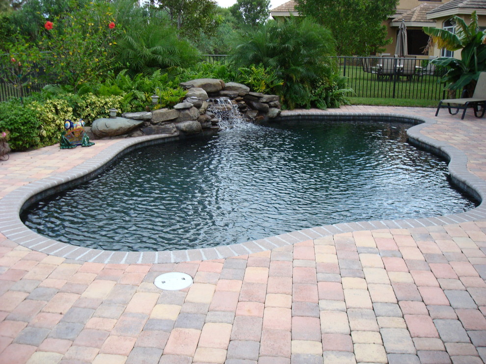 Modelo de piscina con fuente natural exótica grande a medida en patio trasero con adoquines de ladrillo
