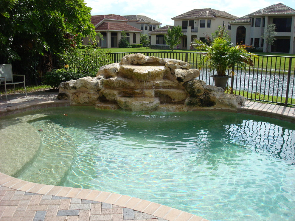 Ejemplo de piscina con fuente natural exótica de tamaño medio a medida en patio trasero con adoquines de ladrillo