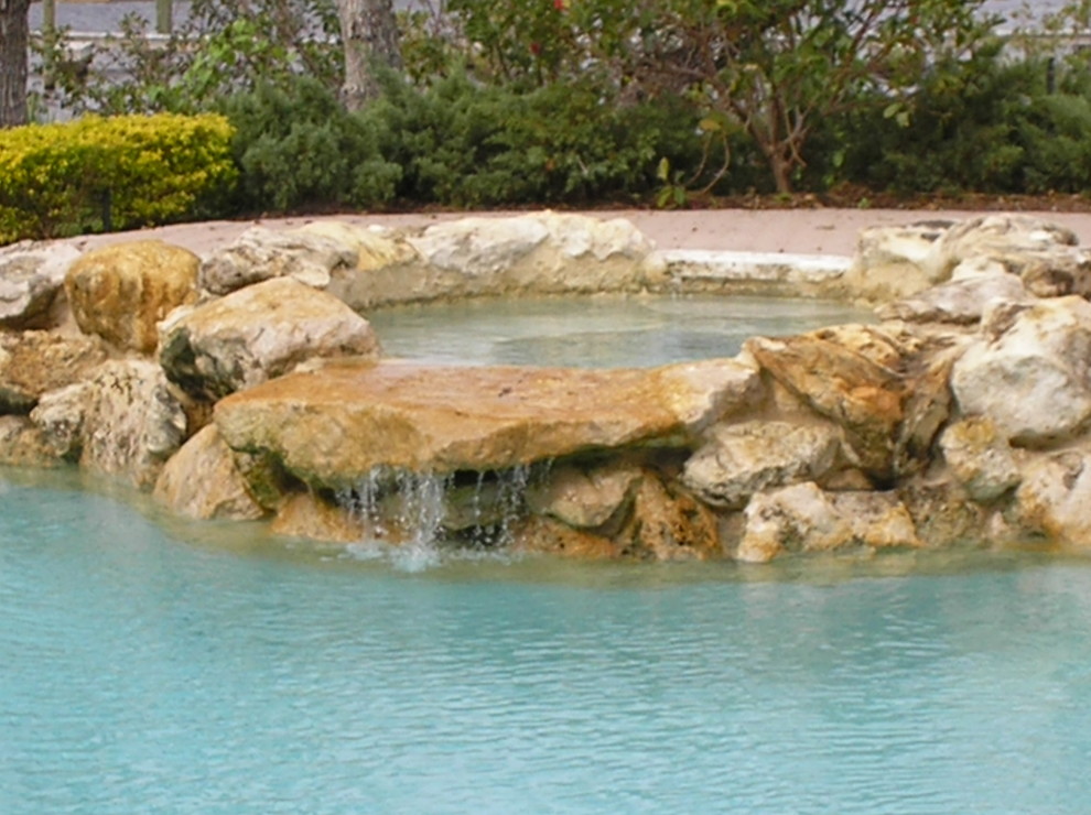 This is an example of a large rustic back custom shaped natural swimming pool in Miami with a water feature.