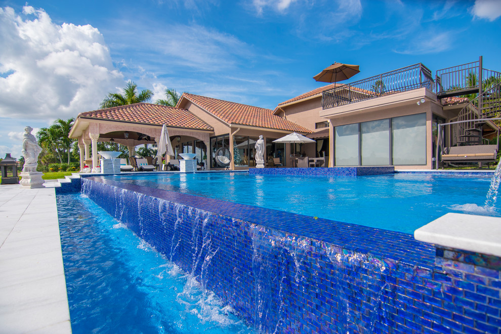 Imagen de piscina alargada minimalista extra grande a medida en patio trasero con adoquines de piedra natural
