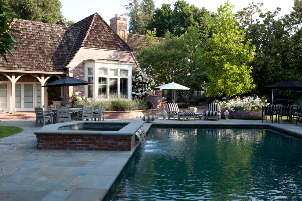 Imagen de piscina clásica de tamaño medio rectangular en patio trasero con paisajismo de piscina y adoquines de piedra natural