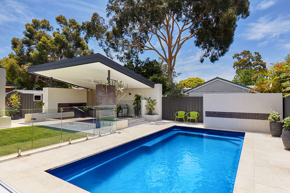 Modelo de piscina actual de tamaño medio rectangular en patio trasero con adoquines de piedra natural