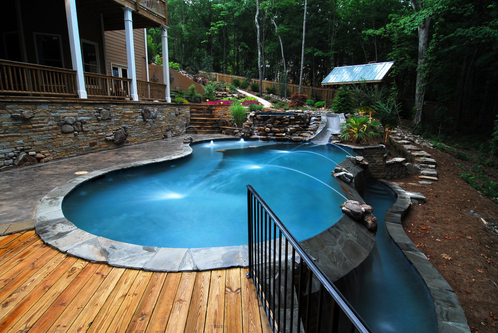 Ejemplo de piscina con tobogán infinita rústica grande tipo riñón en patio trasero con suelo de hormigón estampado