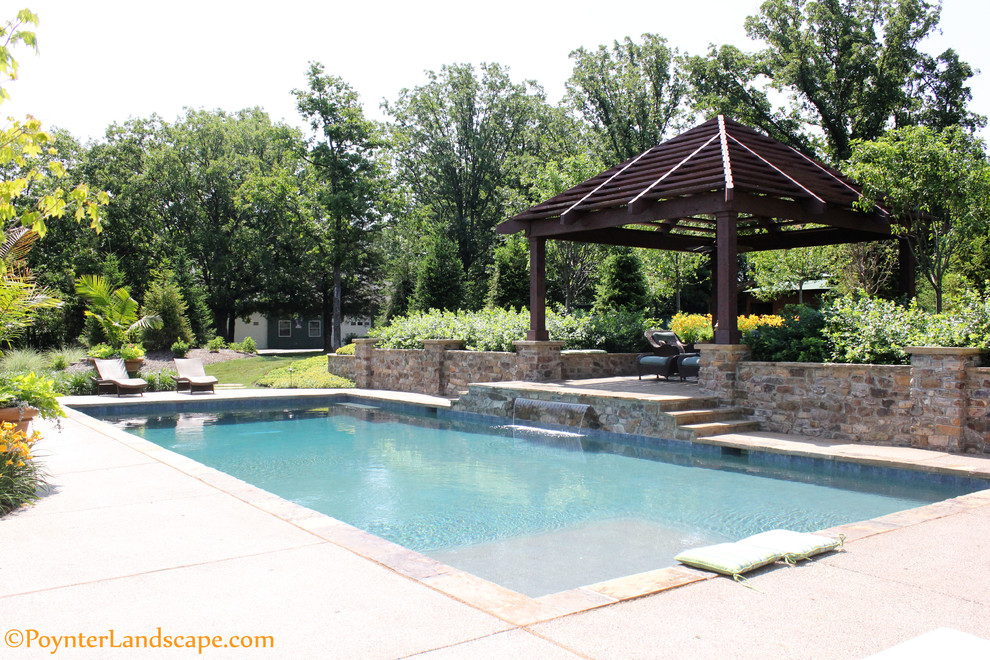 Large country back rectangular natural swimming pool in St Louis with a water feature and concrete slabs.