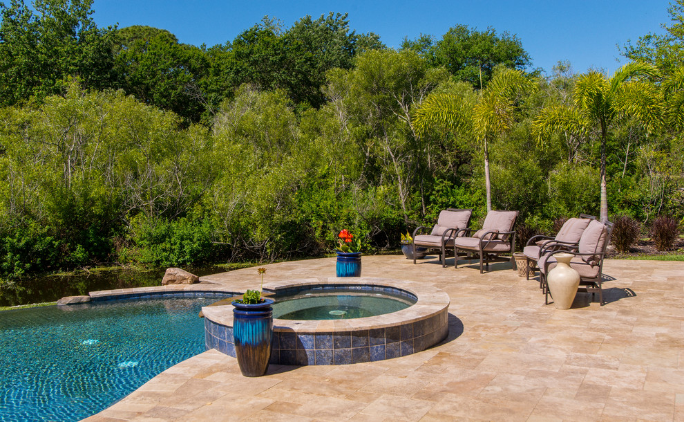 Exemple d'une grande piscine à débordement et arrière chic en forme de haricot avec un bain bouillonnant et des pavés en pierre naturelle.
