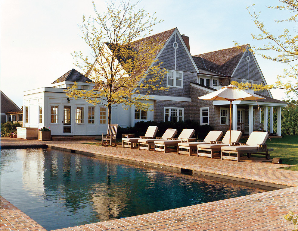 Ejemplo de piscina clásica grande rectangular en patio trasero con adoquines de ladrillo
