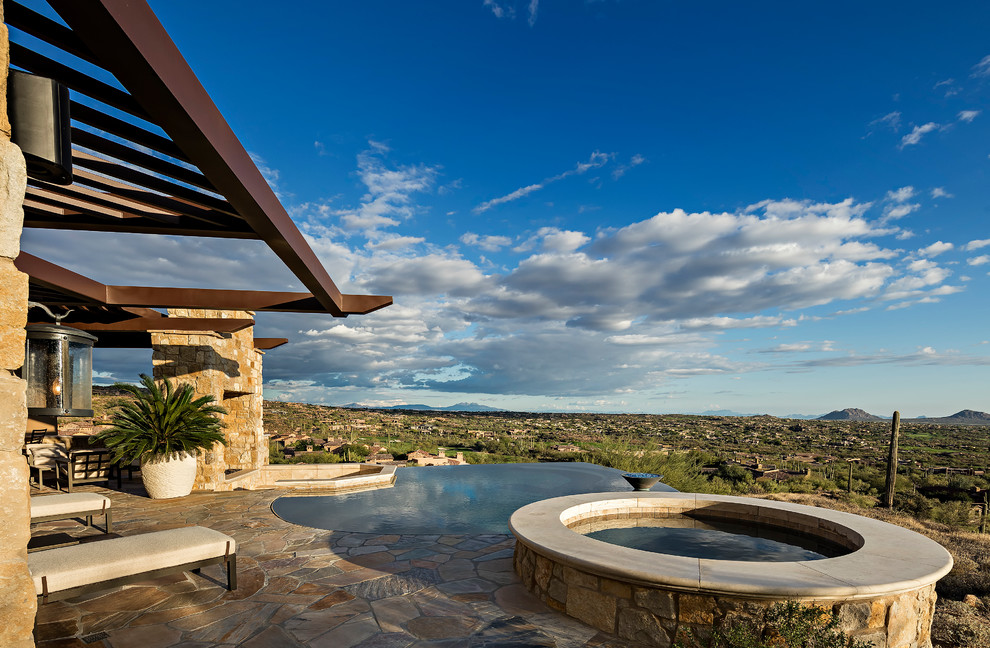 Foto di una grande piscina a sfioro infinito minimal personalizzata dietro casa con una vasca idromassaggio e pavimentazioni in pietra naturale