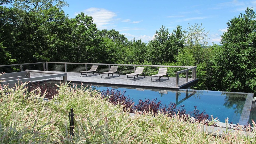 Foto di una grande piscina a sfioro infinito minimalista rettangolare dietro casa con pedane